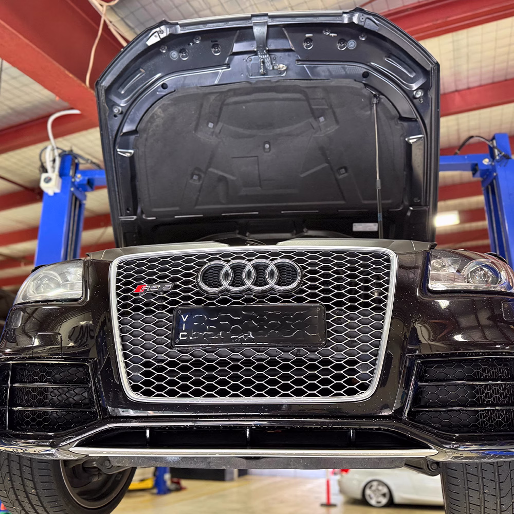 Black Audi RS vehicle on a hoist at the BM Tech workshop with the bonnet open for servicing.