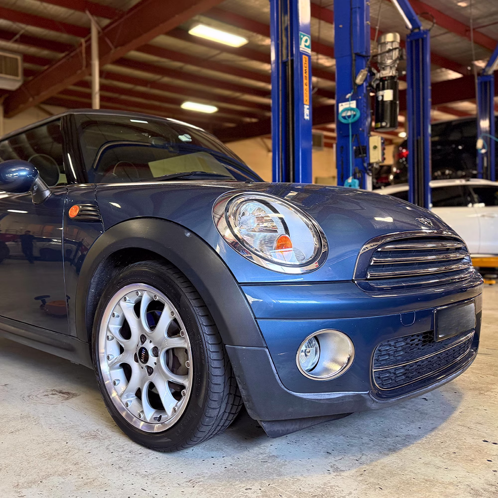 Blue MINI Cooper parked inside an automotive workshop beside a vehicle hoist.