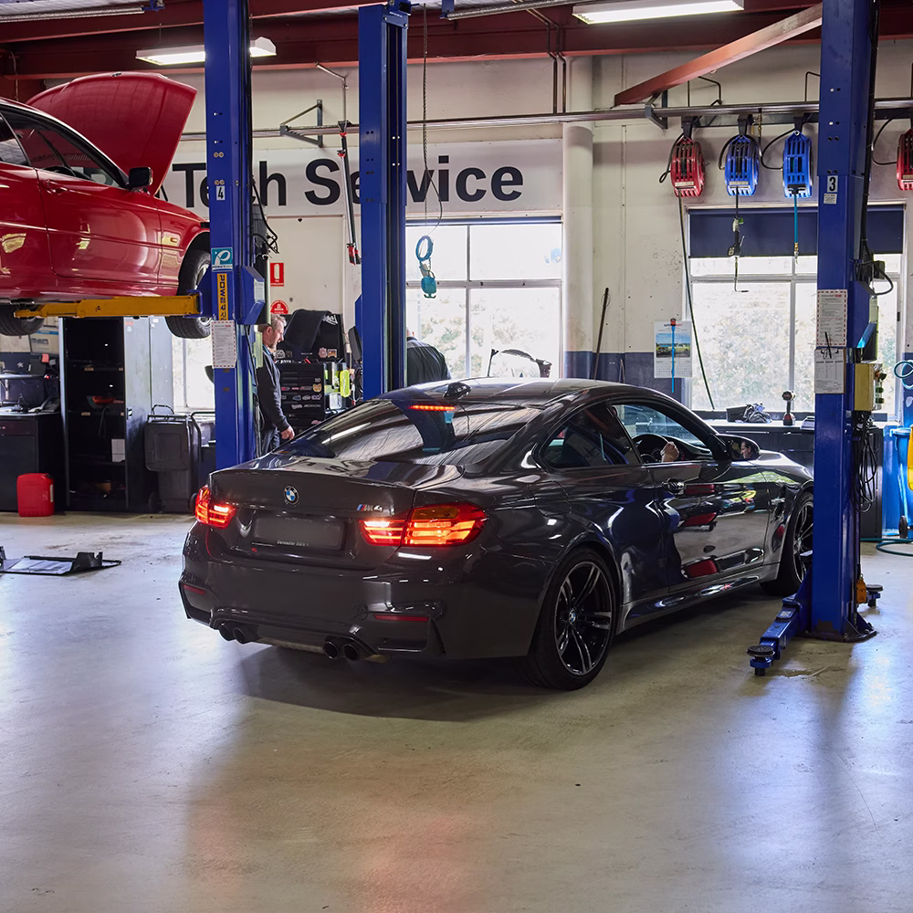 BMW M4 inside the BM Tech workshop, surrounded by vehicle hoists and service equipment.