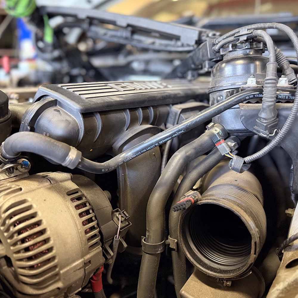 Close-up of a BMW engine bay showing the alternator, intake components, hoses and wiring.