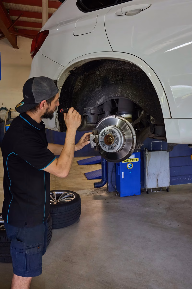 BMT Technician inspecting brake components on a lifted car in the BMT Workshop