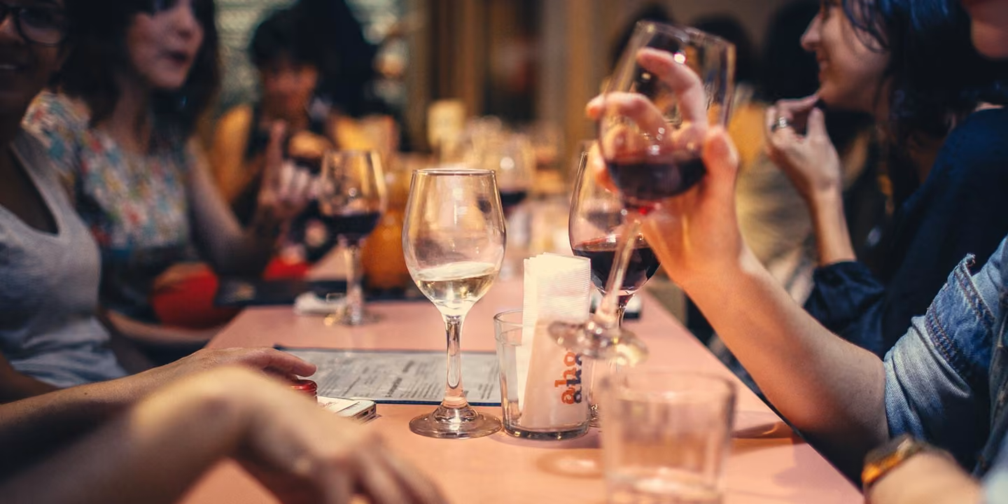 Pessoas em volta de uma mesa em um bar, segurando taças de vinho tinto e branco.