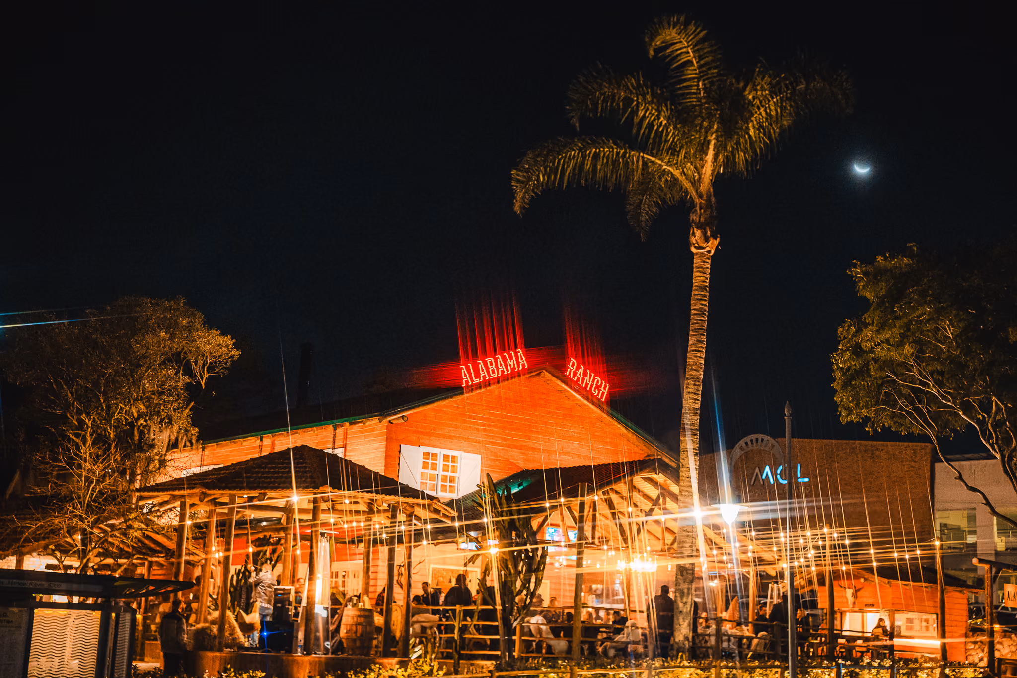 Restaurante Alabama Ranch iluminado à noite com palmeira e céu escuro ao fundo.