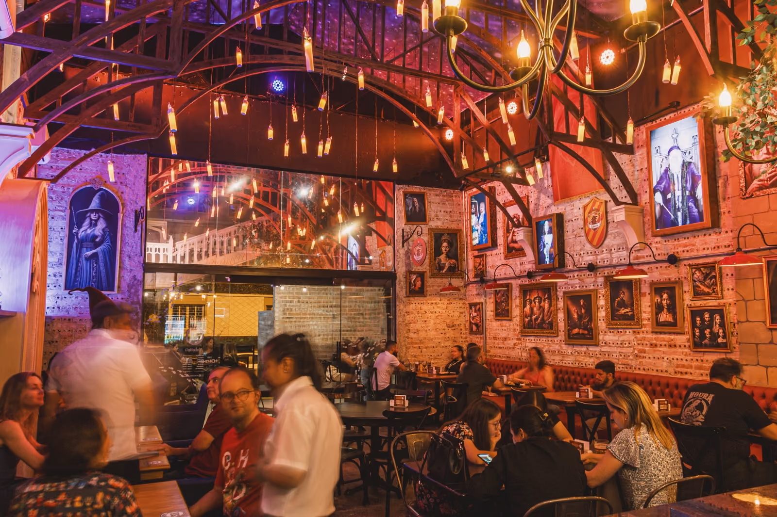 Interior de bar rústico com clientes, iluminação quente e quadros decorativos em paredes de tijolos.