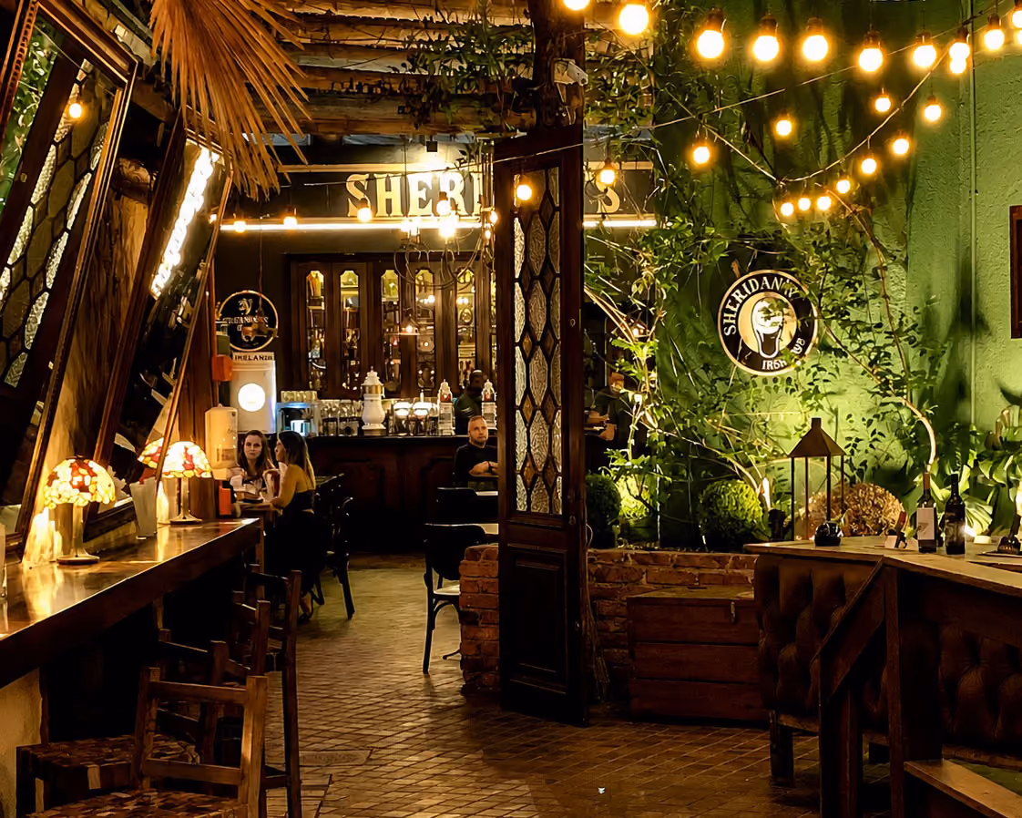 Ambiente interno de pub com decoração aconchegante, luzes pendentes e pessoas sentadas em mesas.