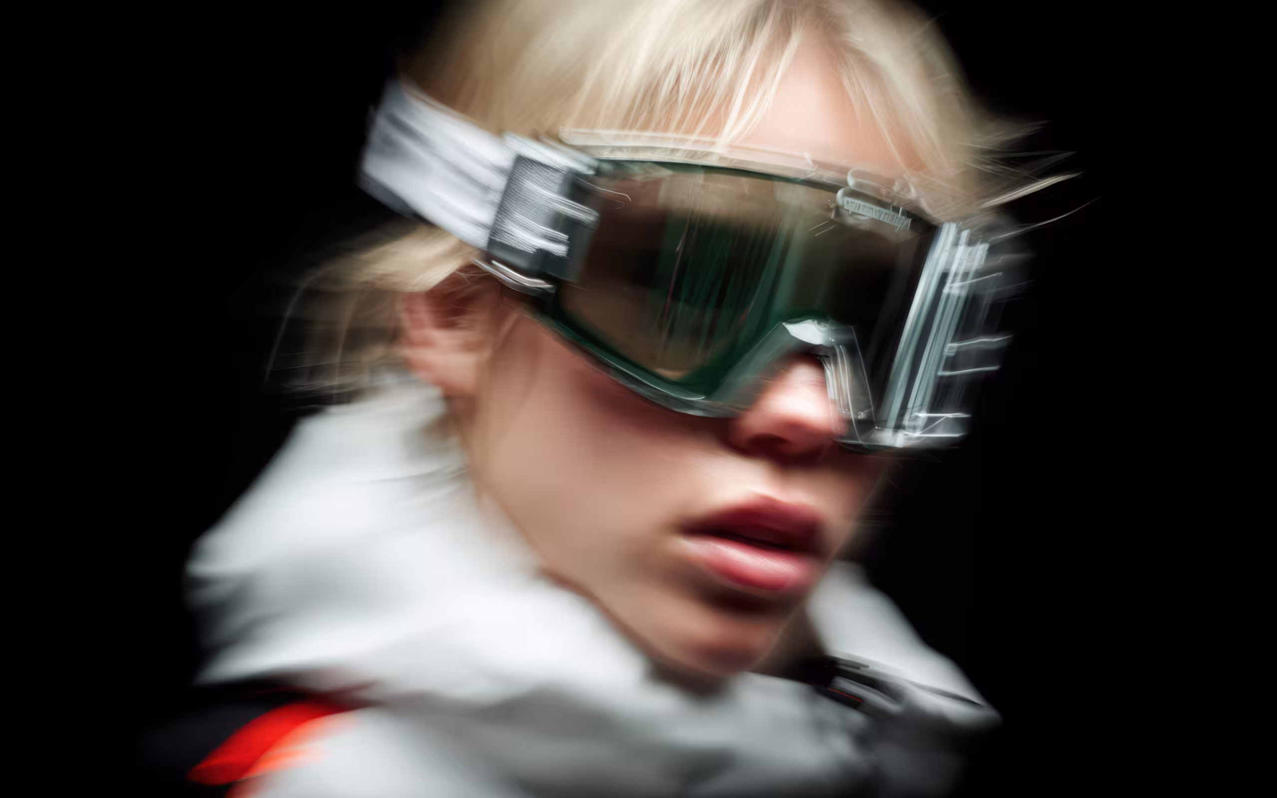 Blurred close-up of a person wearing large protective goggles and a white jacket against a black background.