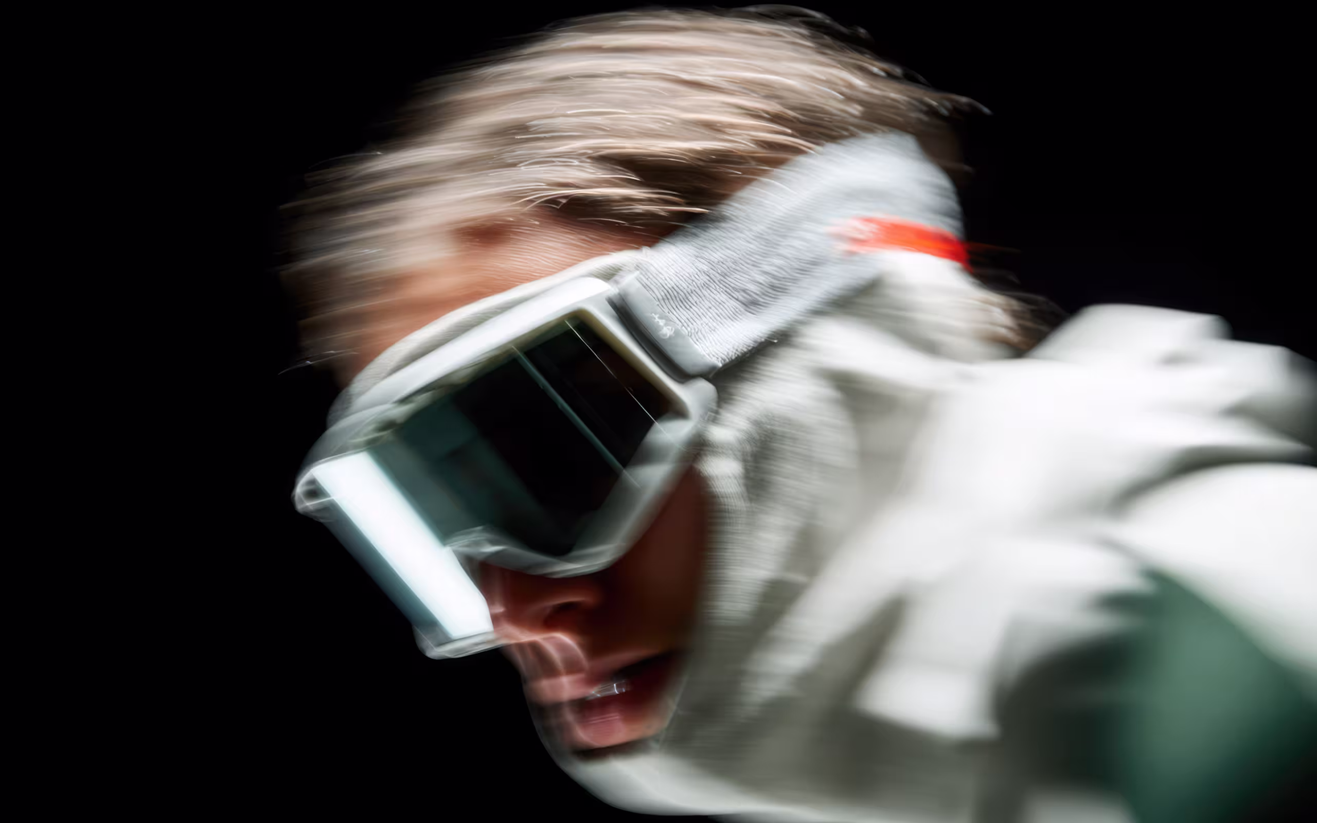 Blurred close-up of a person wearing large protective goggles and a white jacket against a black background.