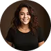 Smiling woman with curly hair wearing a black top against a dark background.