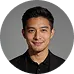 Portrait of a smiling young man with short dark hair and wearing a black collared shirt.