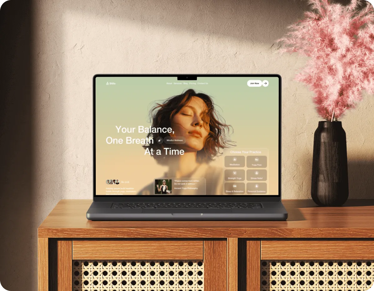 Laptop on wooden cabinet showing wellness website with a woman's face and balance message, next to pink flowers.