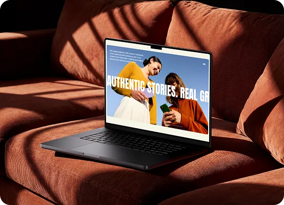 Laptop on a rust-colored sofa displaying a webpage with two women and large text reading 'Authentic Stories.'