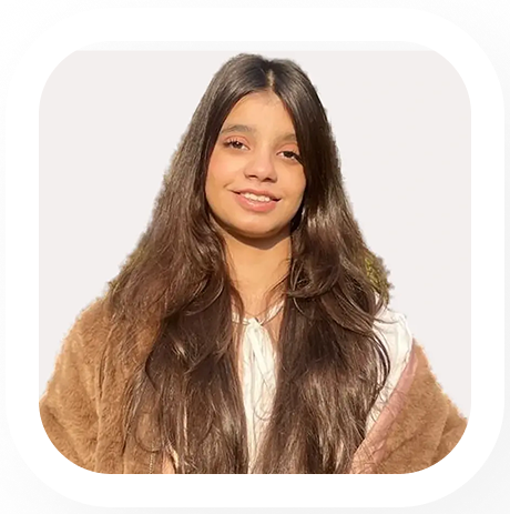 Smiling young woman with long brown hair wearing a white top and a brown furry jacket.