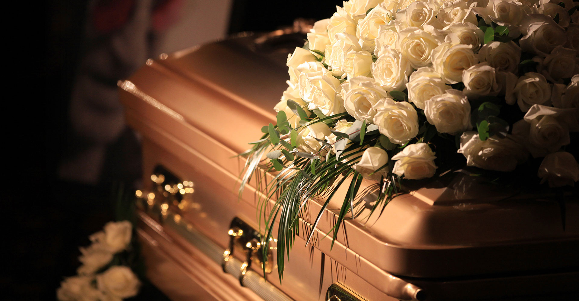 Bronze casket with a large arrangement of white roses and greenery