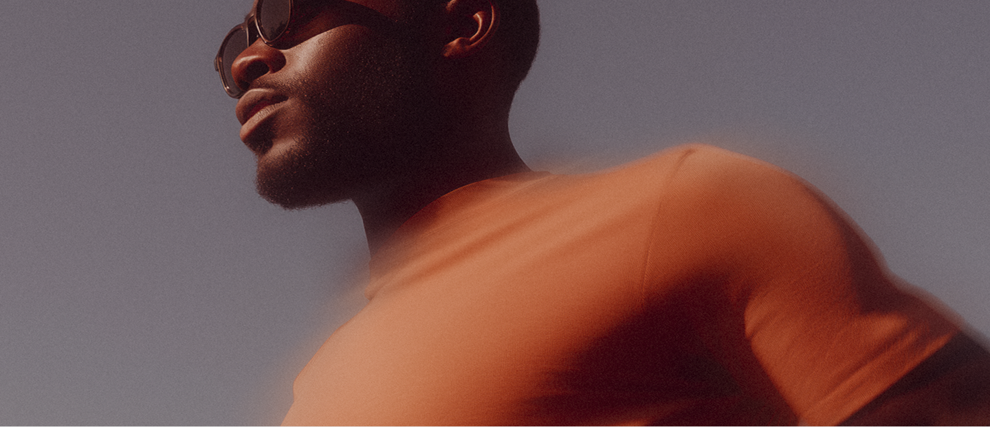 Portrait of a man wearing sunglasses and an orange shirt against a clear sky.