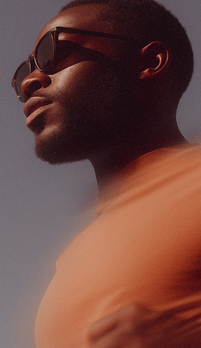 Portrait of a man wearing dark sunglasses and an orange shirt against a muted background.