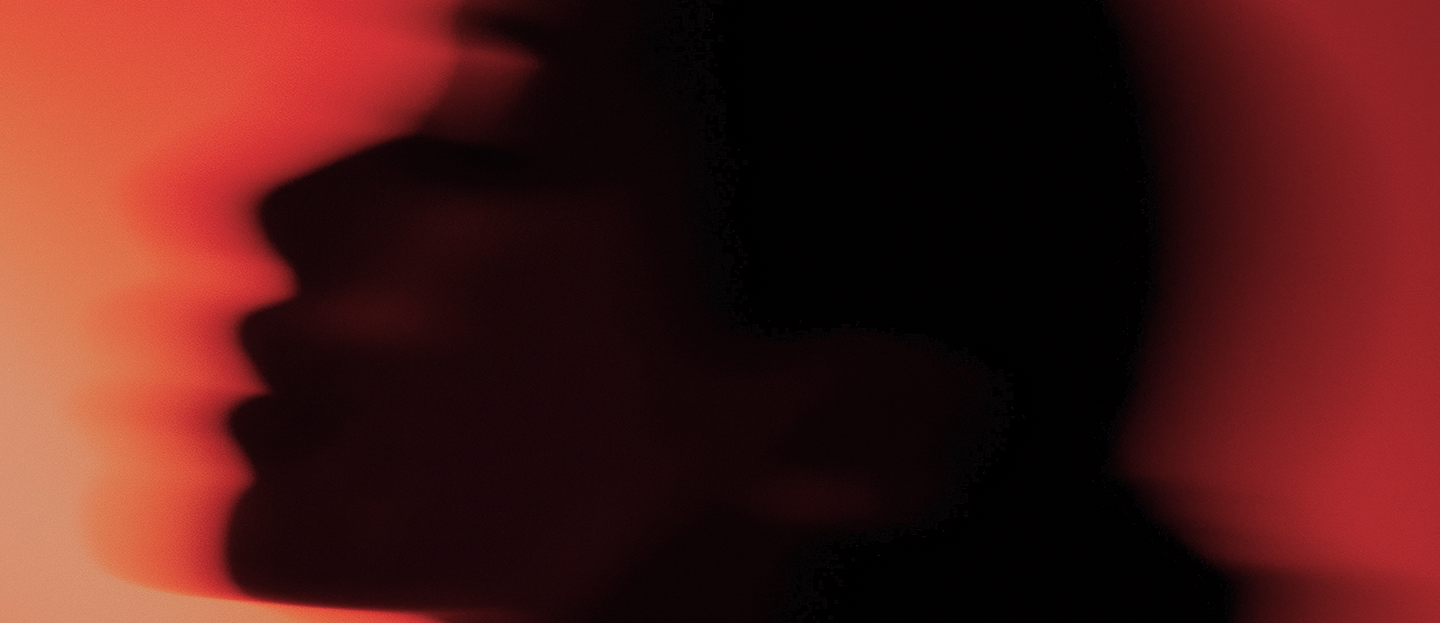 Blurred silhouette of a face in profile against a red background.