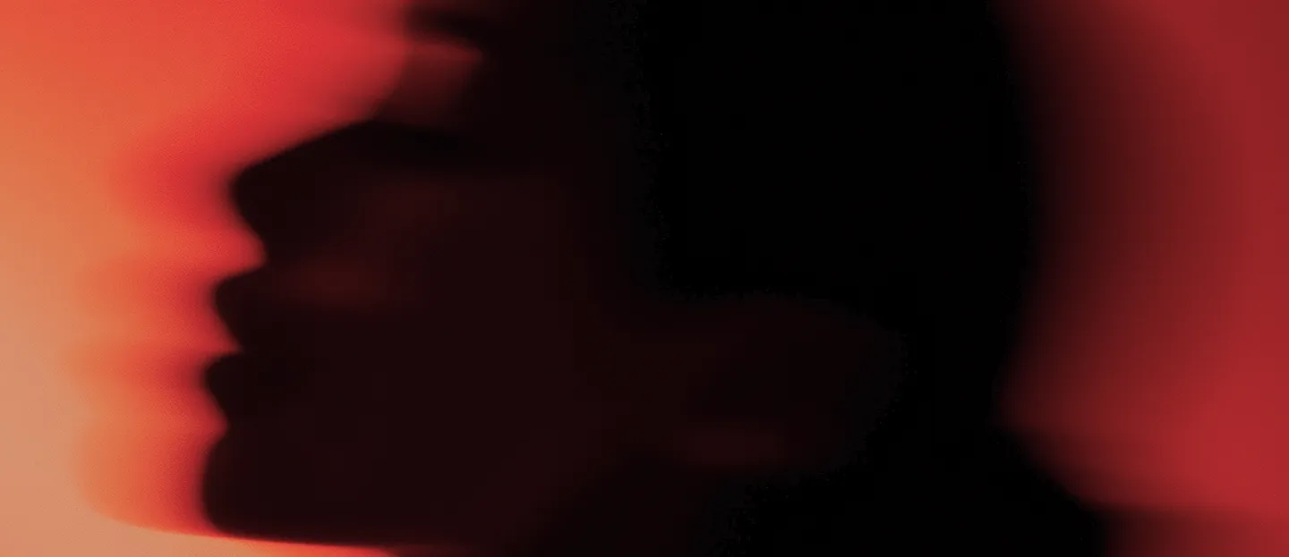 Blurred silhouette of a face in profile against a red background.