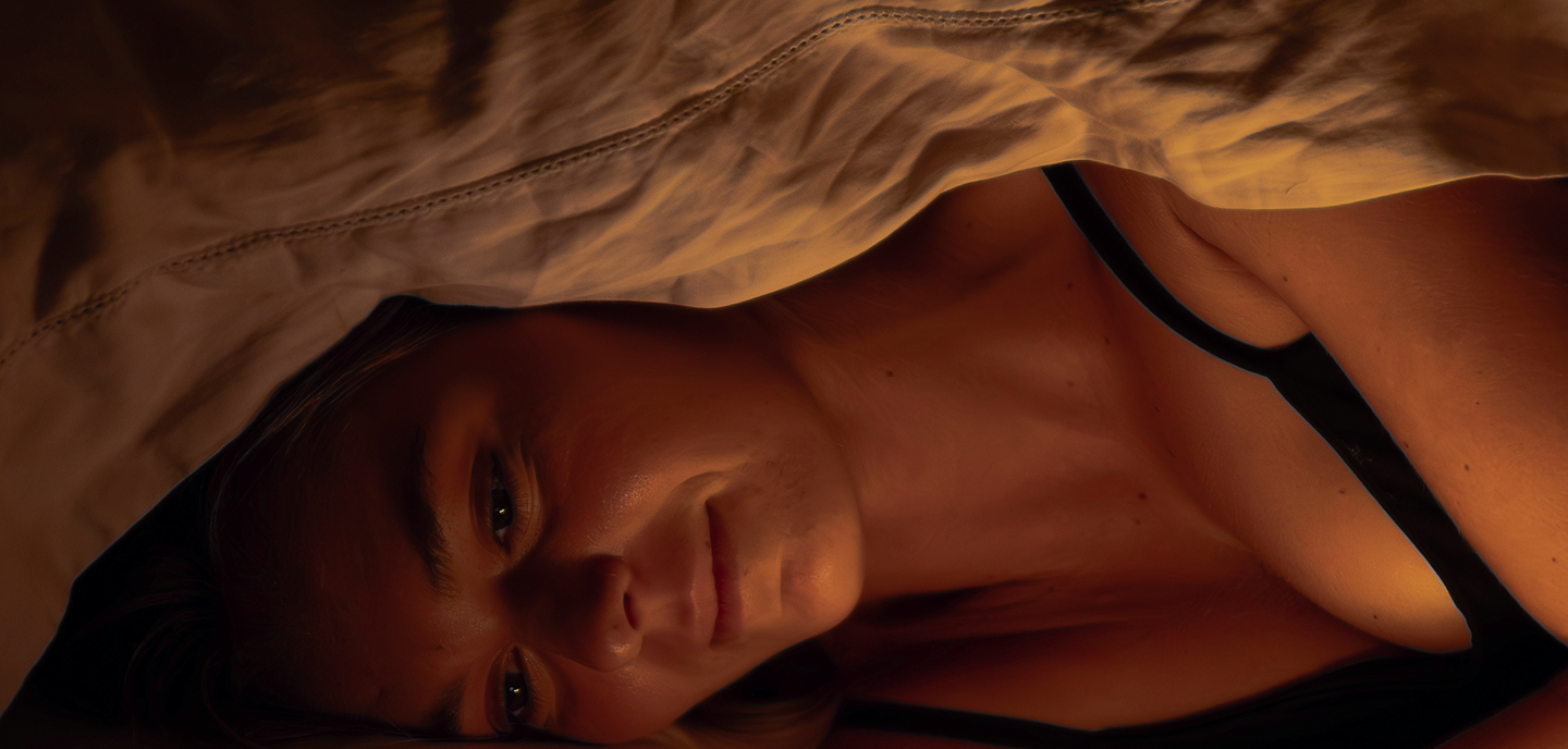 Woman lying down under a blanket with warm soft lighting on her face and shoulder.