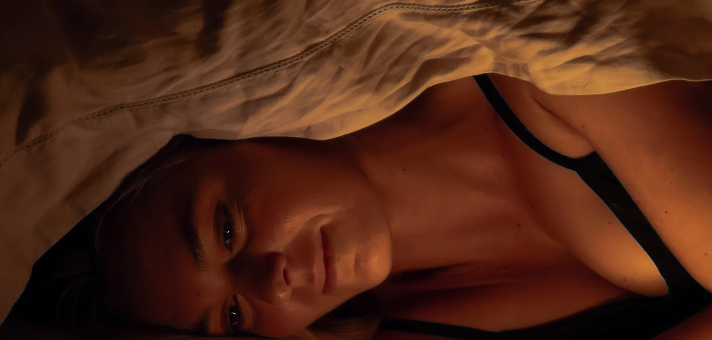 Woman lying down under a blanket with warm soft lighting on her face and shoulder.