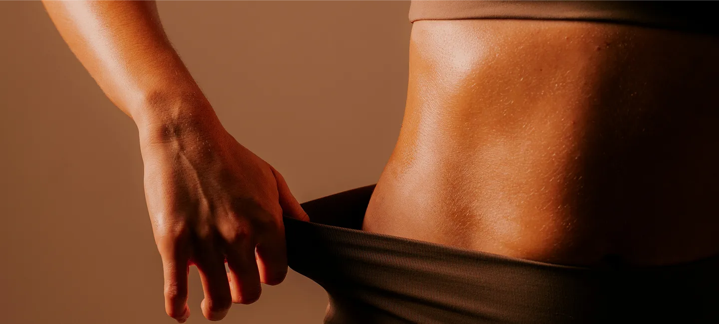 Close-up of a person pulling waistband outward, showing toned abdomen and hand with veins visible.