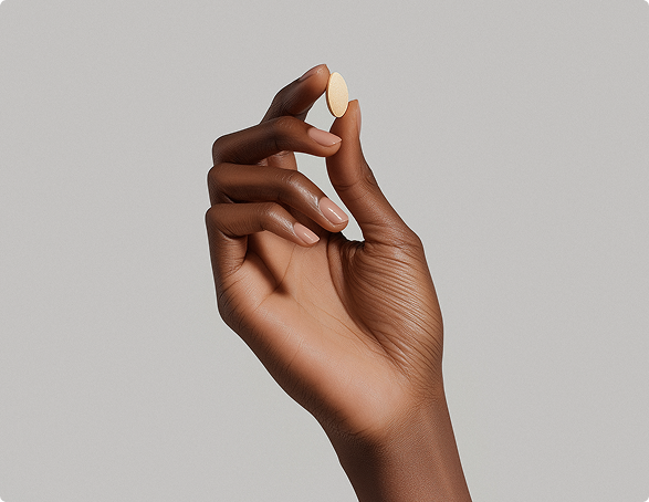 Close-up of a dark-skinned hand holding a yellow capsule against a plain light background.