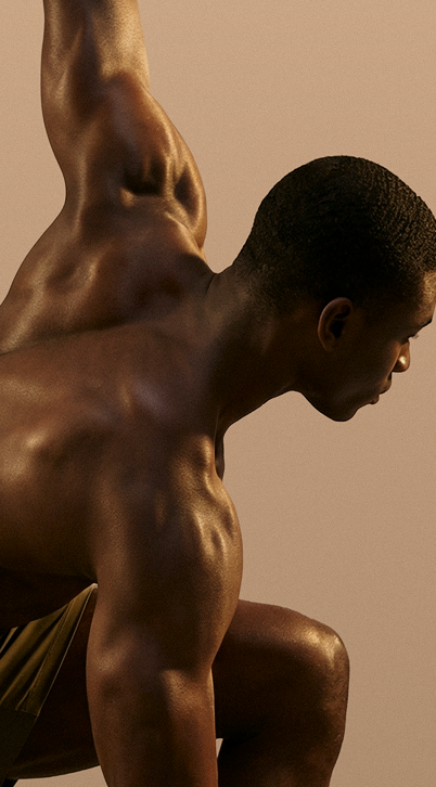 Muscular man in shadowed lighting poses with one arm raised and bent, showing defined back and shoulder muscles.
