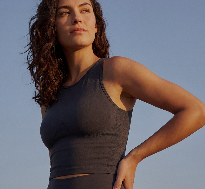 Confident woman in dark activewear standing outdoors with hand on hip under clear blue sky.