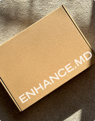 Closed cardboard box with the text ENHANCE.MD on the lid, placed on a textured surface with shadows.