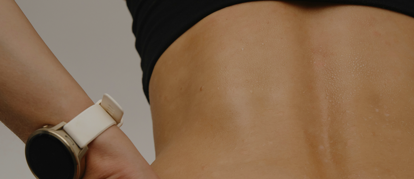 Close-up of a person's sweaty lower back with a smartwatch on their wrist.