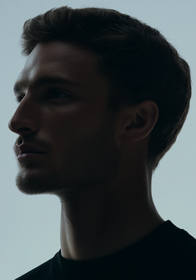 Side profile of a young man with short hair and facial hair against a plain light background.