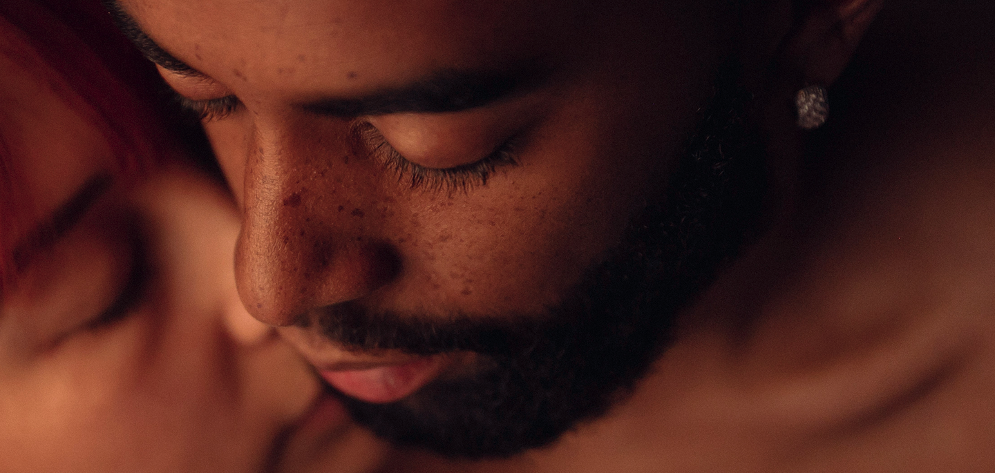 Close-up of a man with eyes closed and a diamond earring, face touching another person.