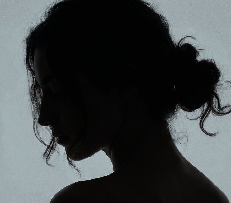 Silhouette of a woman in profile with curly hair tied in a bun against a gray background.