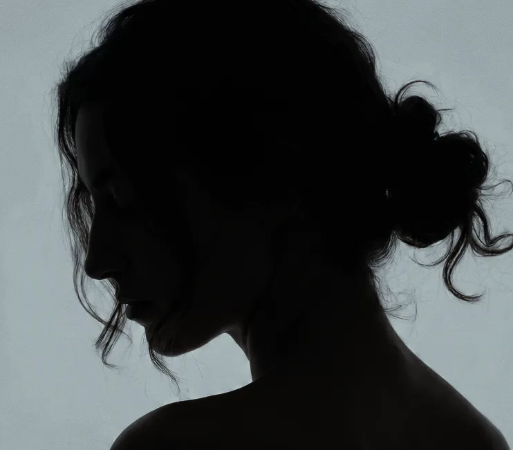 Silhouette of a woman in profile with curly hair tied in a bun against a gray background.