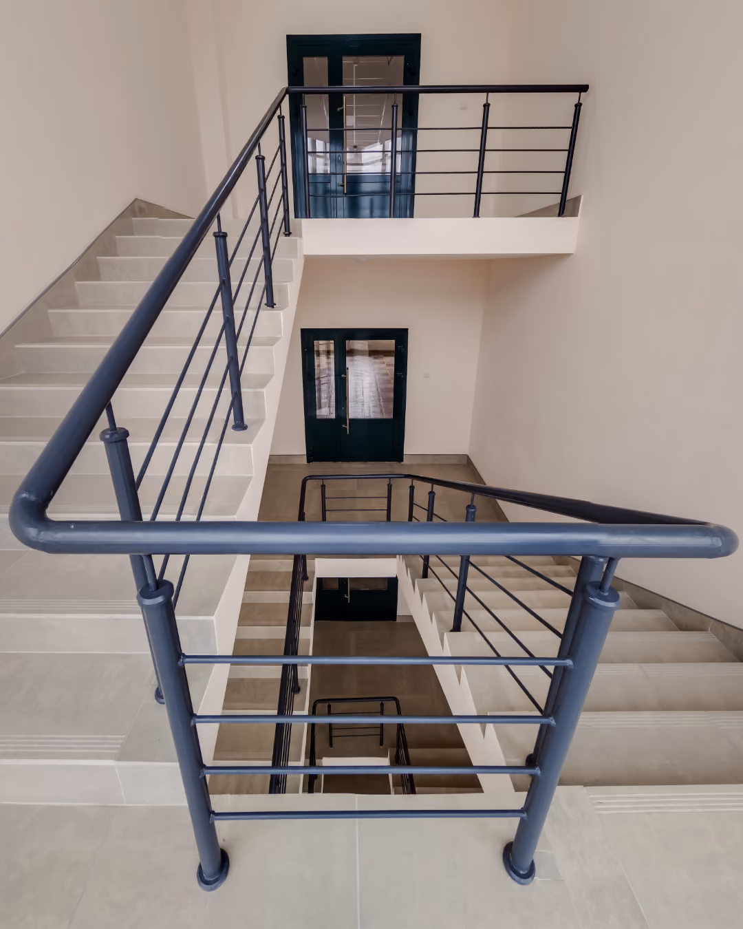 Moderner Innenraum mit hellen Treppen und schwarzen Metallgeländern in einem Gebäudetreppenhaus.