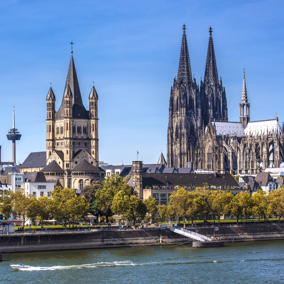 Kölner Dom und Groß Sankt Martin Kirche mit Boot auf dem Rhein unter klarem Himmel.