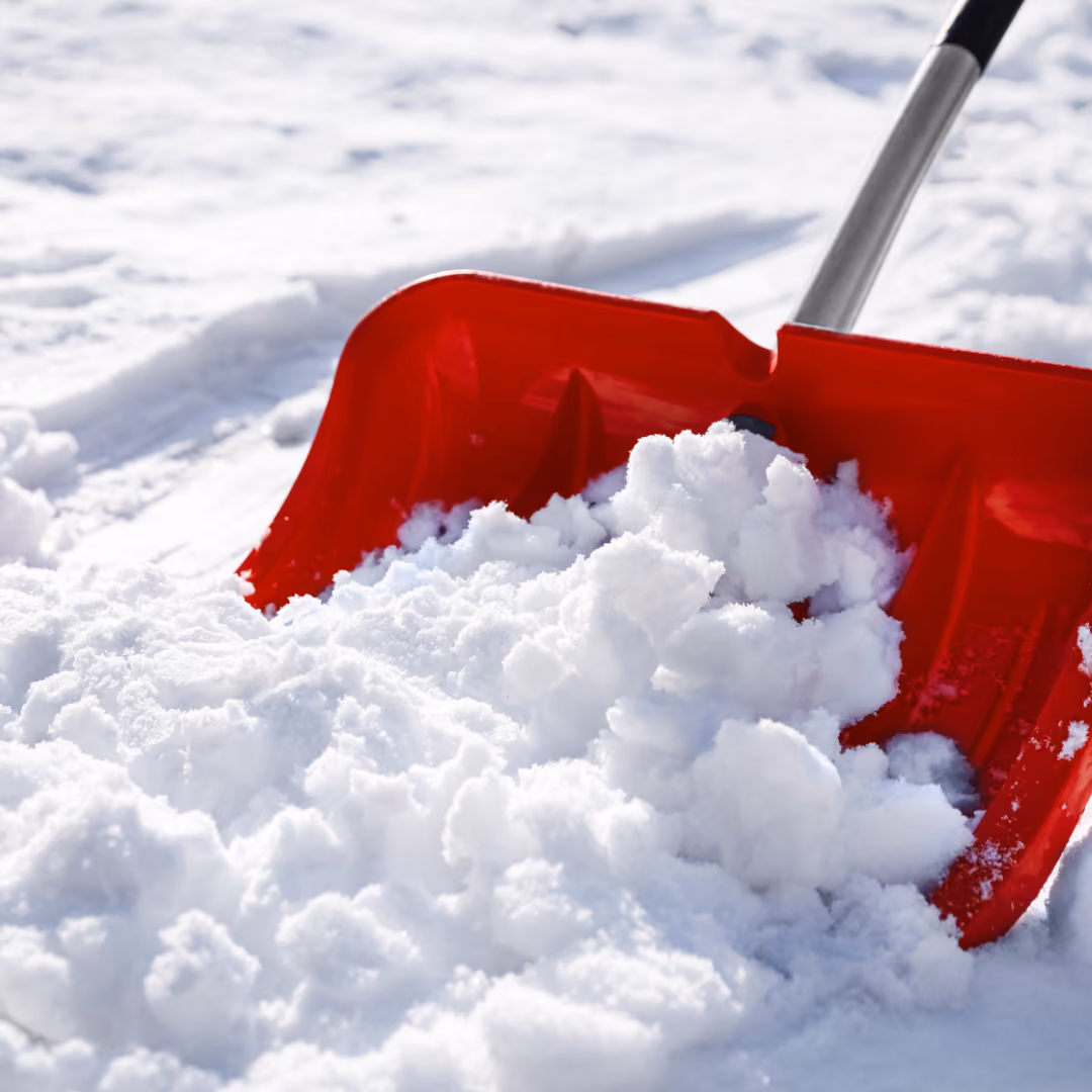 Roter Schneeschieber schaufelt frischen, weißen Schnee auf einem verschneiten Untergrund.