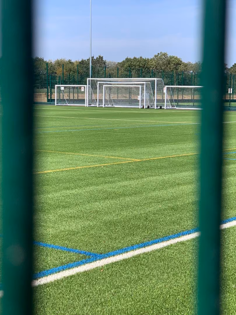 Soccer field with white goals viewed through green fence with marked boundary lines