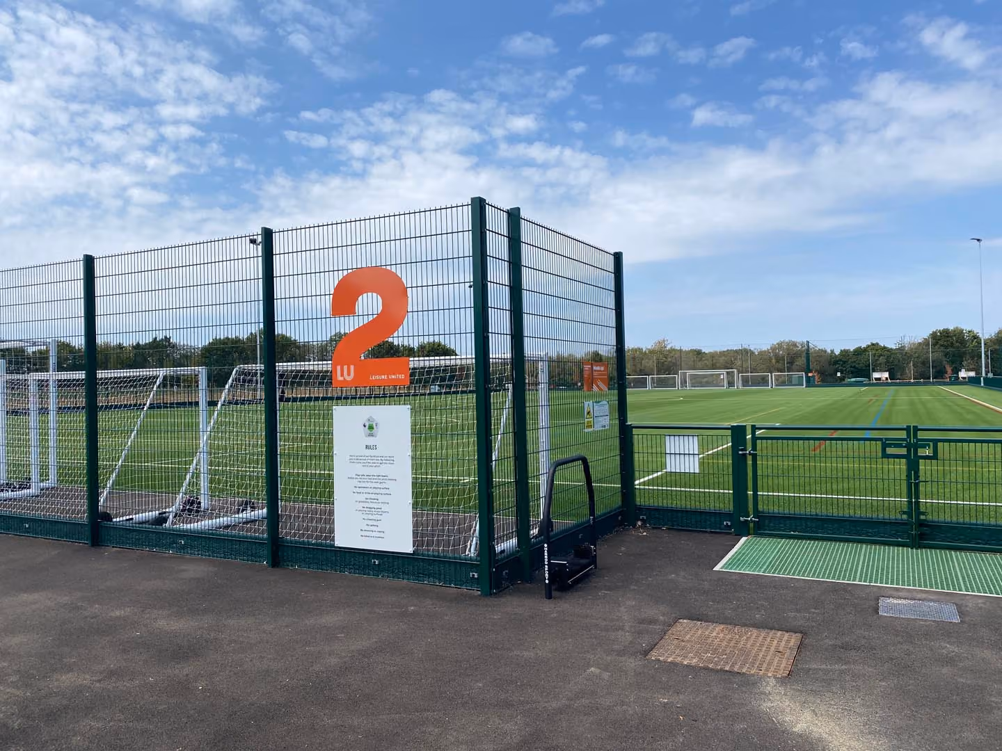 Sports field with green fenced pitch number 2, soccer goals visible under blue sky