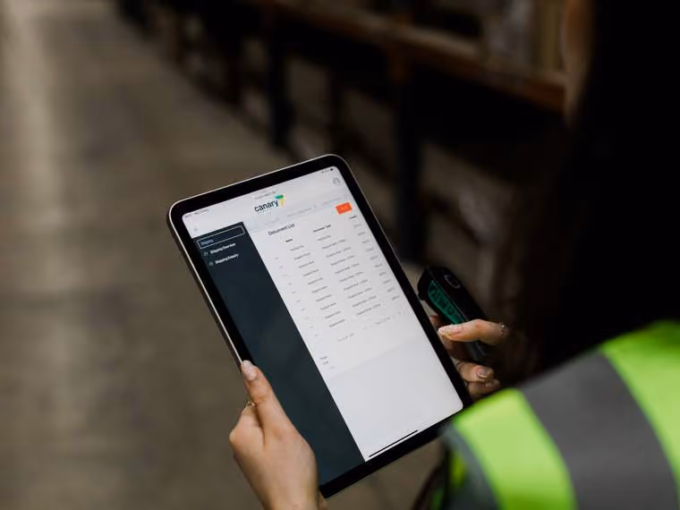 Person wearing a safety vest holding a tablet displaying a digital dashboard with data tables.