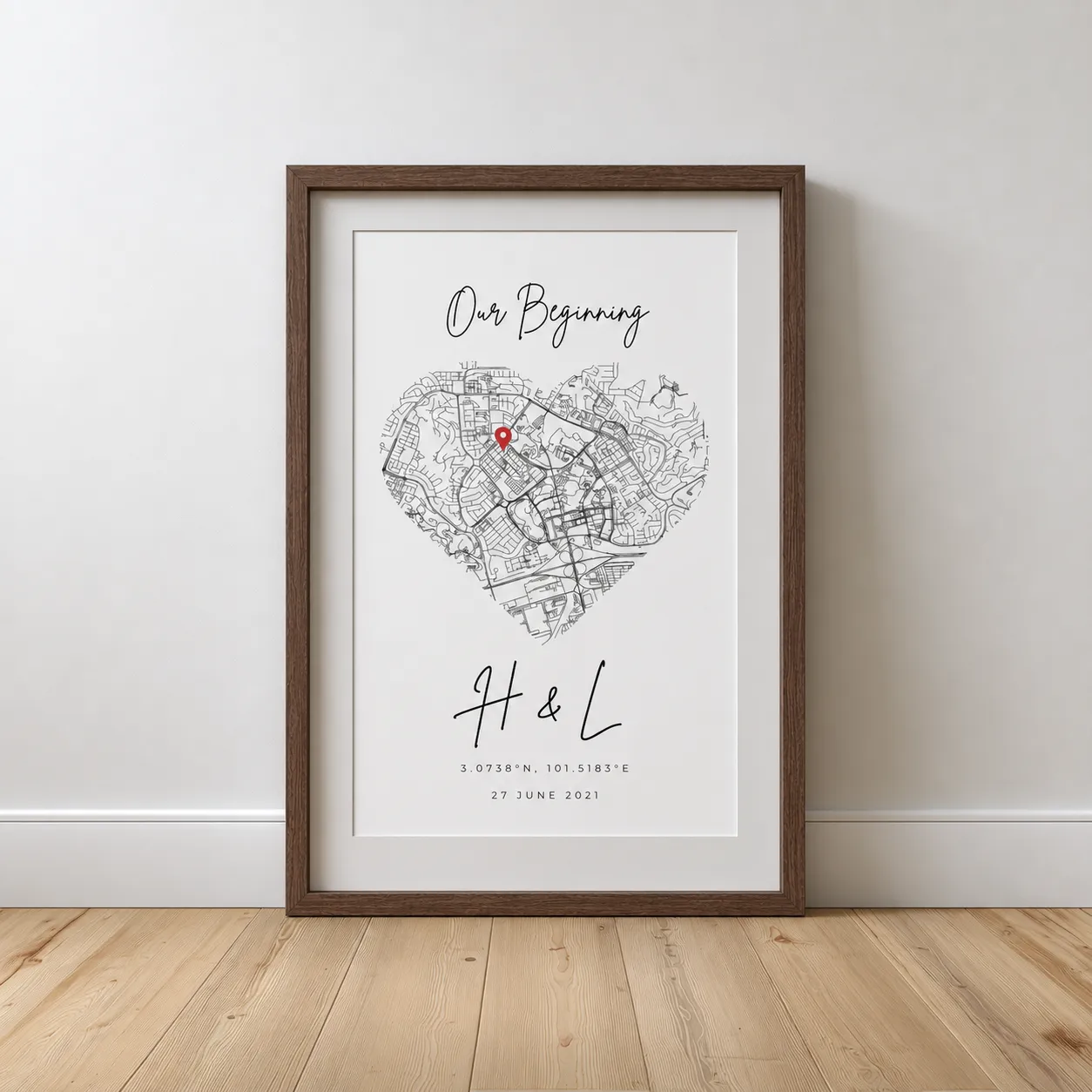 Framed map in heart shape with red location pin, titled Our Beginning with initials H & L and date.