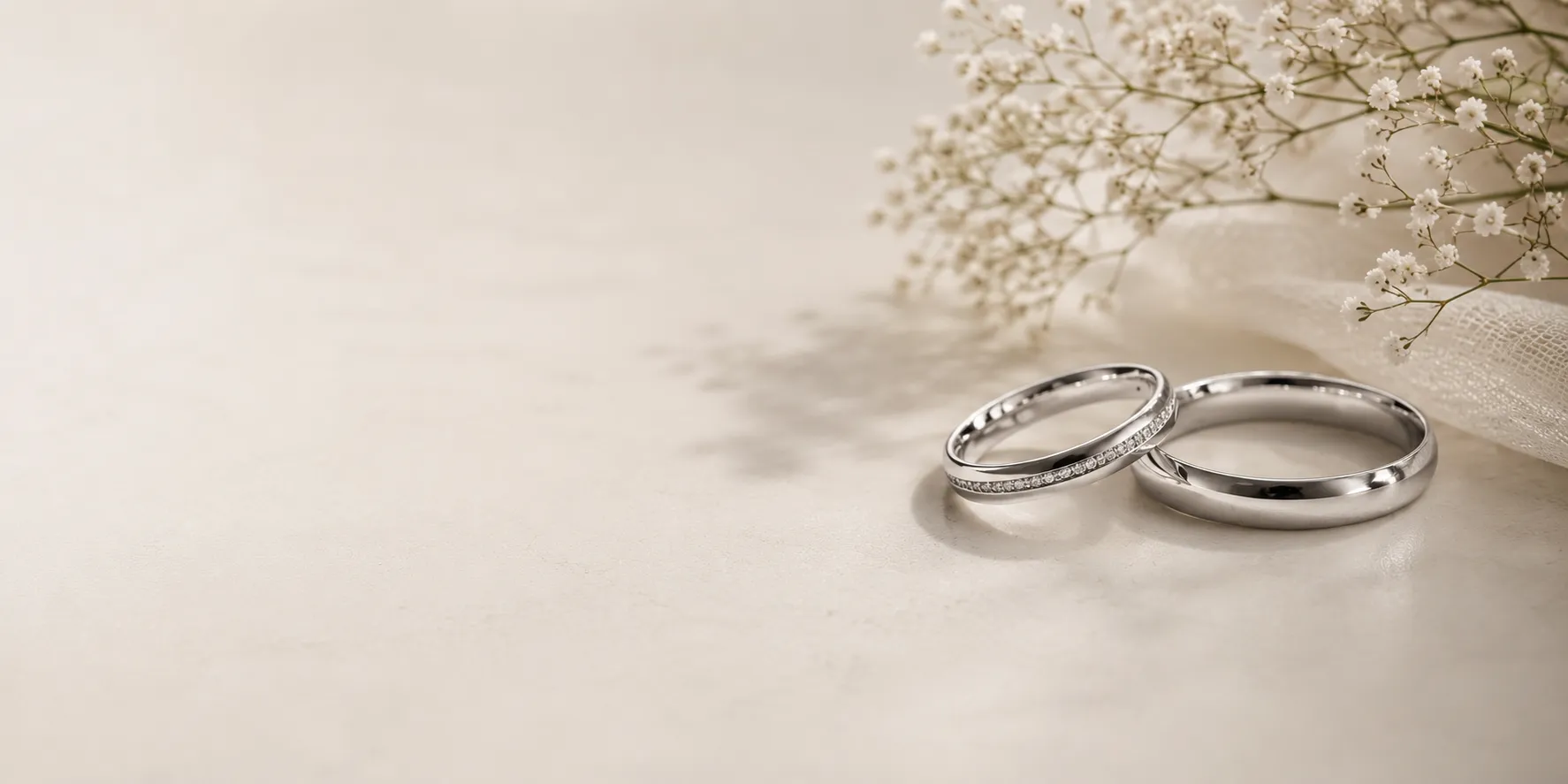 Two silver wedding rings on a smooth surface next to delicate white baby's breath flowers.