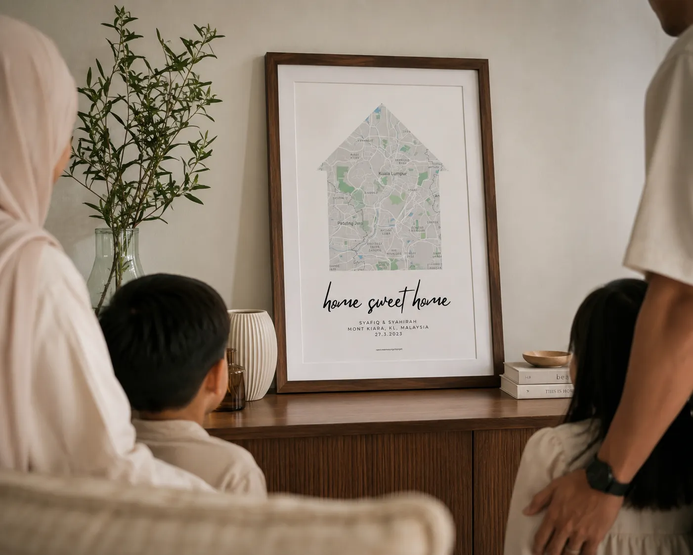 Family of four looking at a framed map art shaped like a house with 'home sweet home' text.