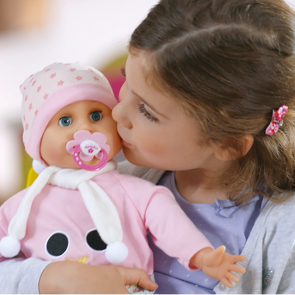 Girl with brown hair kissing a baby doll wearing a pink outfit and white scarf.