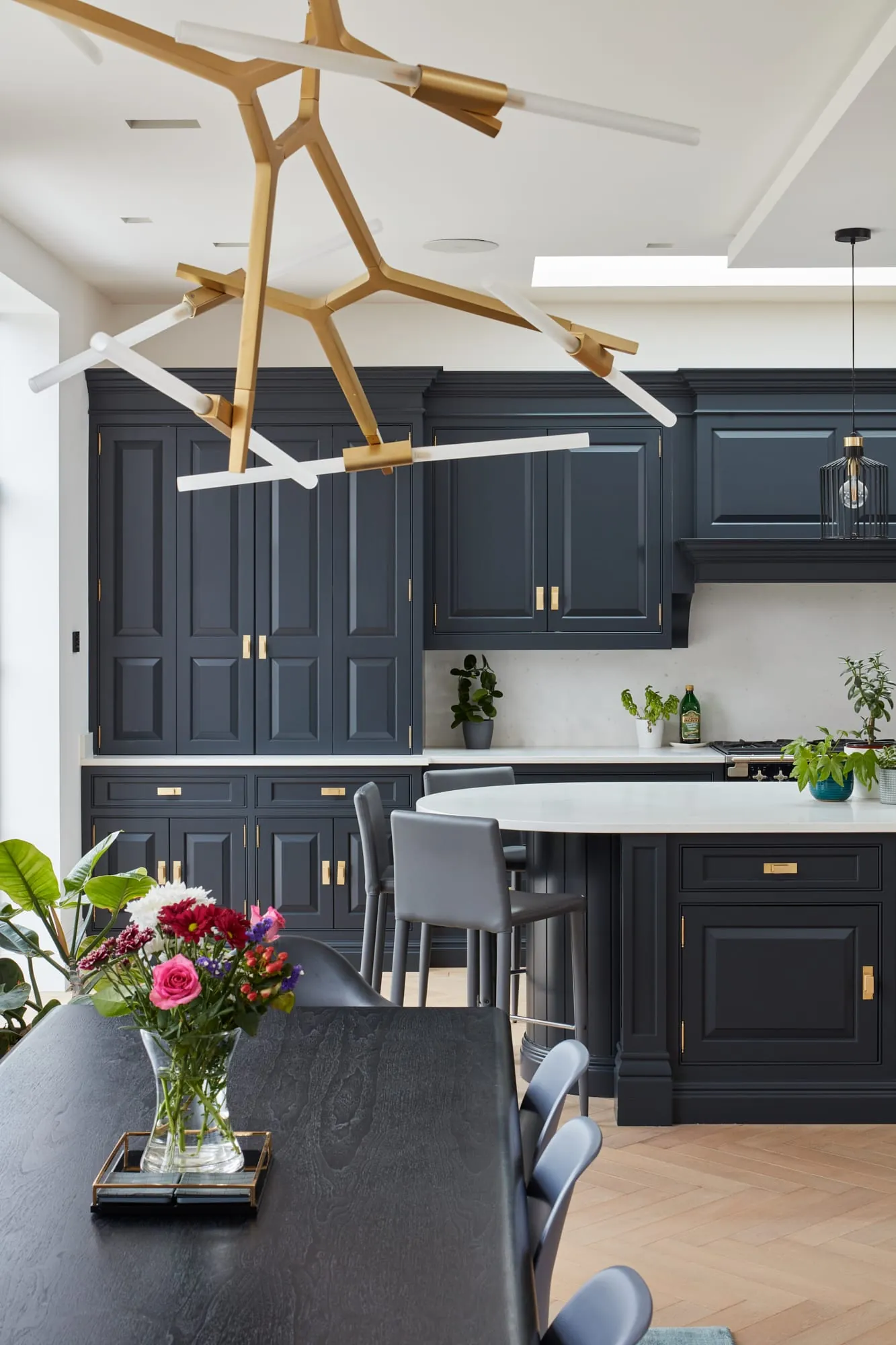 Open-plan kitchen with navy panelled cabinets, a brass branch light and a dining table