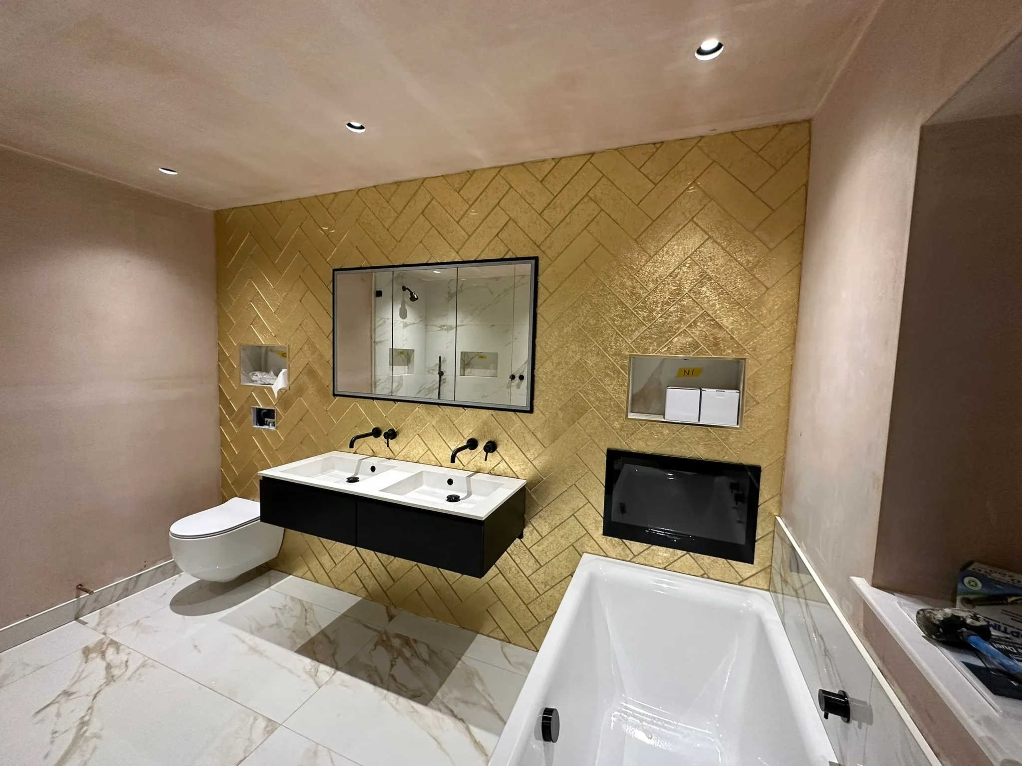 Bathroom with gold herringbone wall tiles, a double vanity, wall-hung WC and marble-effect floor