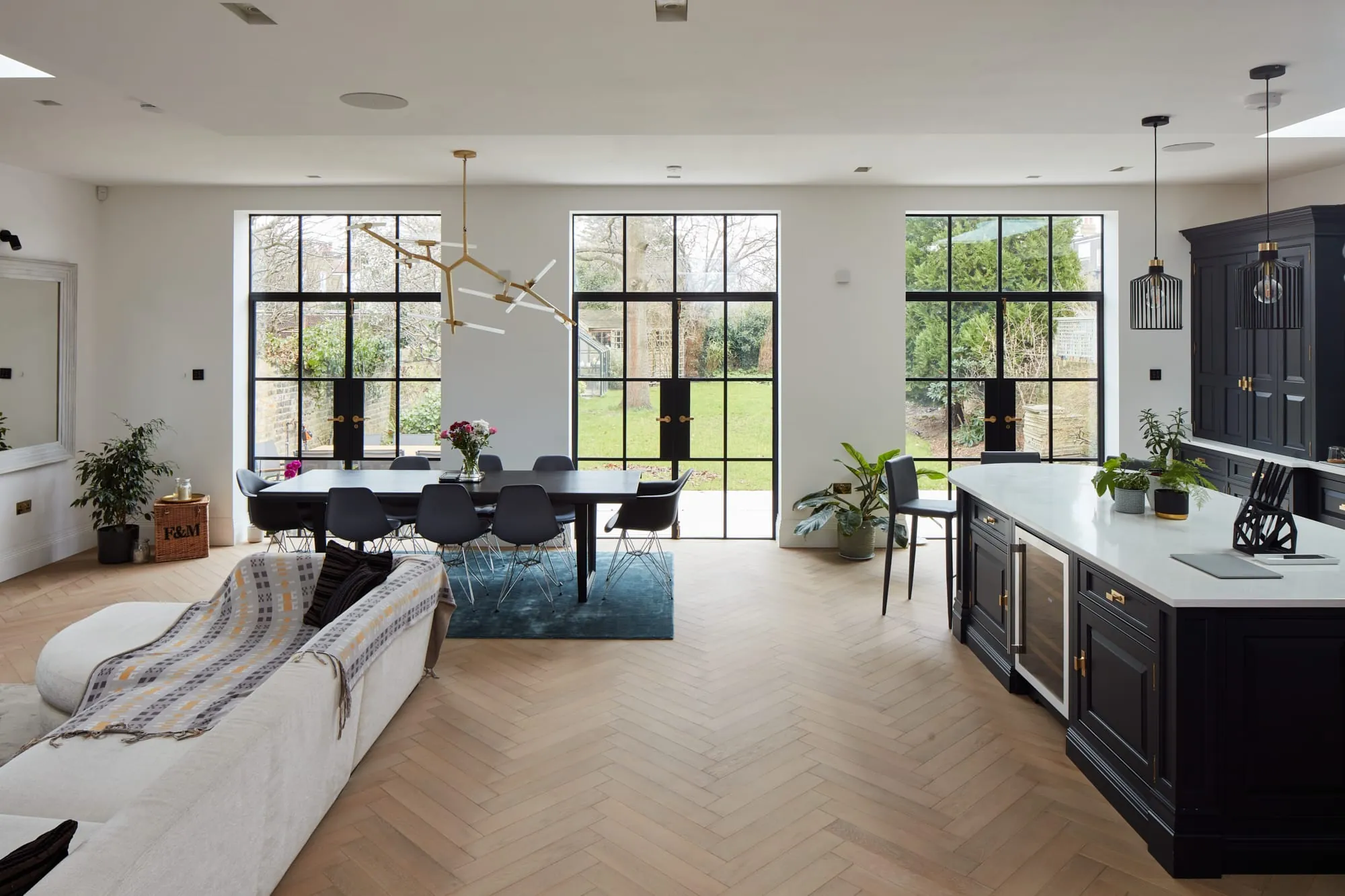Open-plan kitchen, dining and living space with herringbone floor and black steel-framed doors to the garden