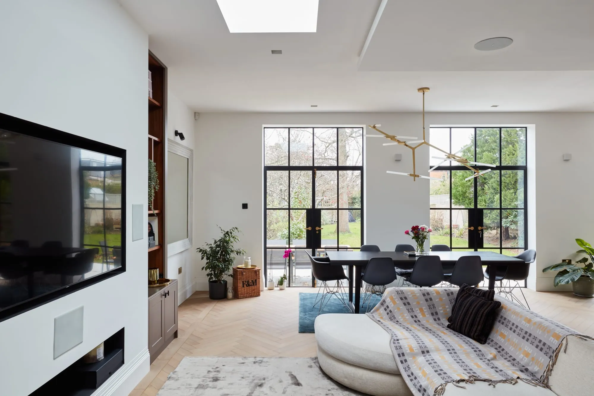 Open-plan living area with a media wall, curved sofa and steel-framed doors to the garden