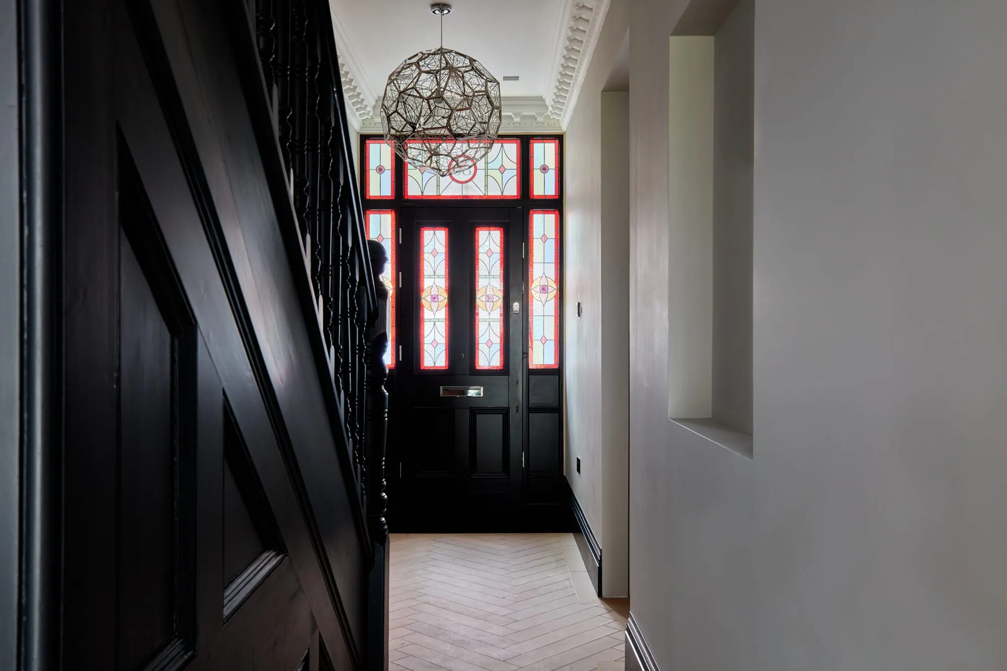 Victorian hallway with a stained glass front door, black painted staircase and herringbone floor
