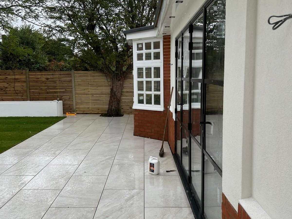 Pale porcelain patio laid right up to the glazed doors and brick plinth