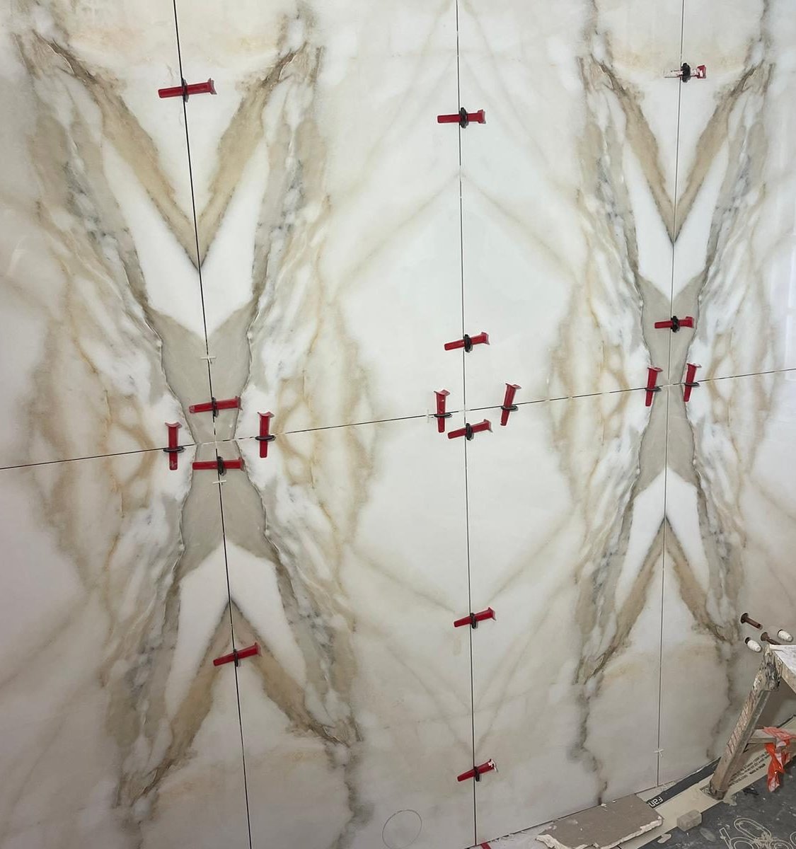 Book-matched marble-effect wall tiles being fitted, with red levelling clips at the joints